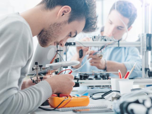 Two young men working on a machinery at a desk